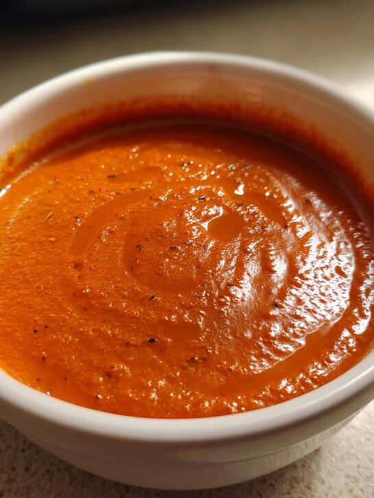 Close-up of a white bowl filled with rich, orange-red Creamy Roasted Garlic Tomato Soup.