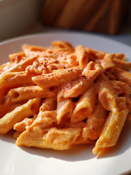 Close-up of penne pasta generously coated in creamy orange Vodka Sauce, sprinkled with red pepper flakes.