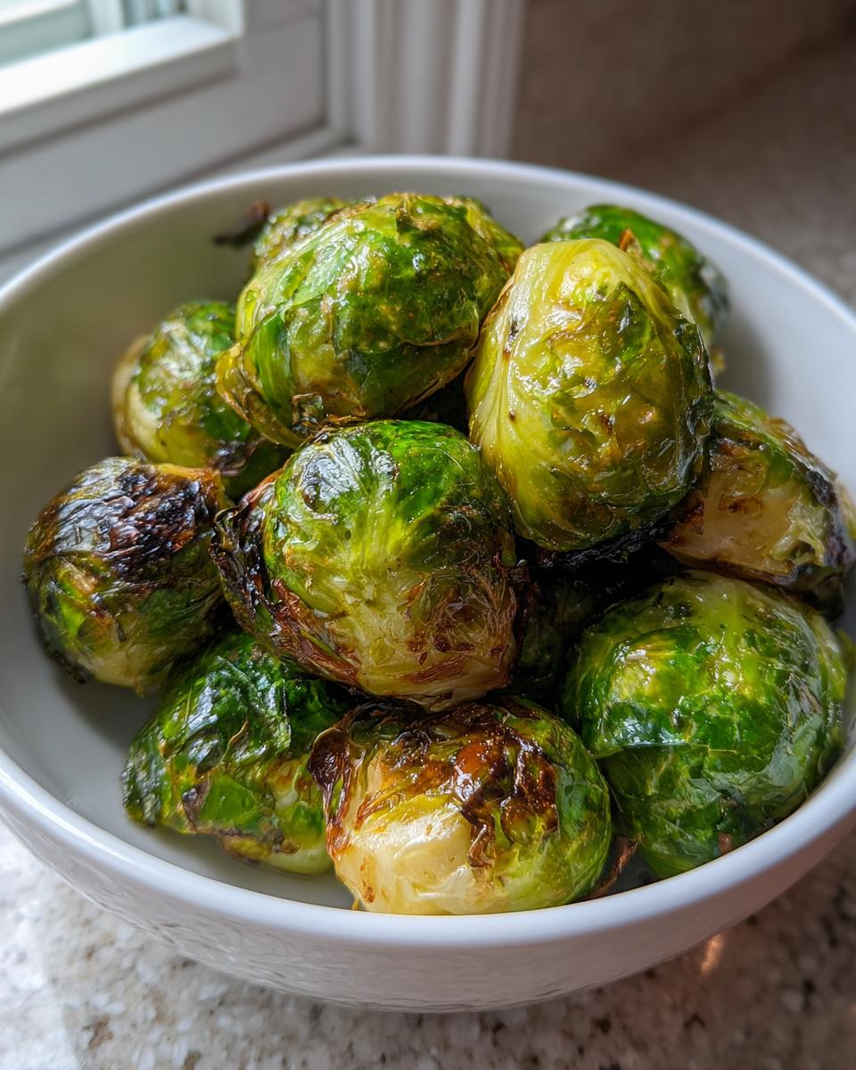 A close-up of crispy, slightly charred Air Fryer Brussels Sprouts piled high in a white serving bowl.