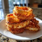 A stack of golden brown, perfectly textured Crispy Baked Onion Rings piled on a white plate.