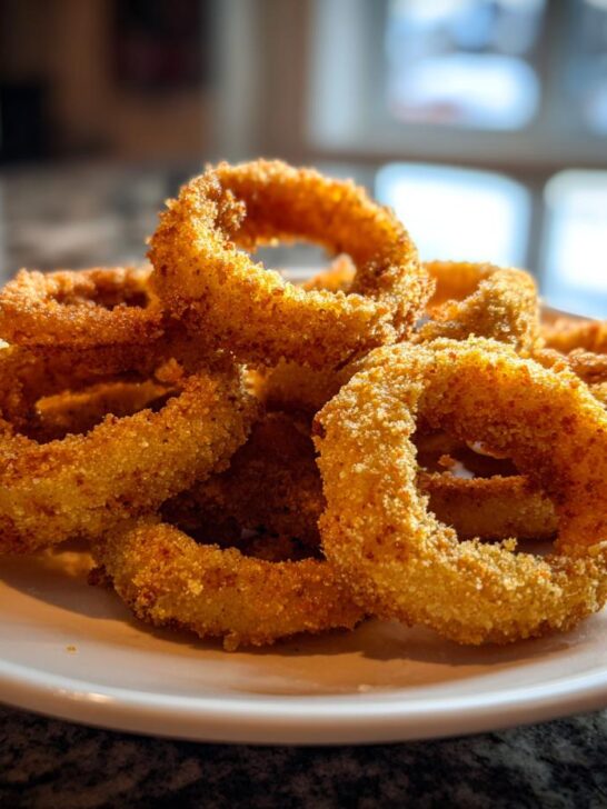 A close-up of a pile of golden brown, perfectly breaded Crispy Baked Onion Rings on a white plate.