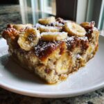A square slice of moist Crock Pot Creamy Banana French Toast topped with fresh banana slices and powdered sugar.