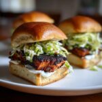 A close-up of one of the Easy Blackened Salmon Sliders featuring blackened fish, creamy sauce, and coleslaw on a brioche bun.