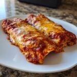 Two baked Easy Chicken Enchiladas covered in rich red sauce and melted golden cheese on a white plate.
