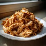 A mound of flavorful, seasoned Easy Shredded Chicken Recipe Seasoned Gold piled high on a white plate.