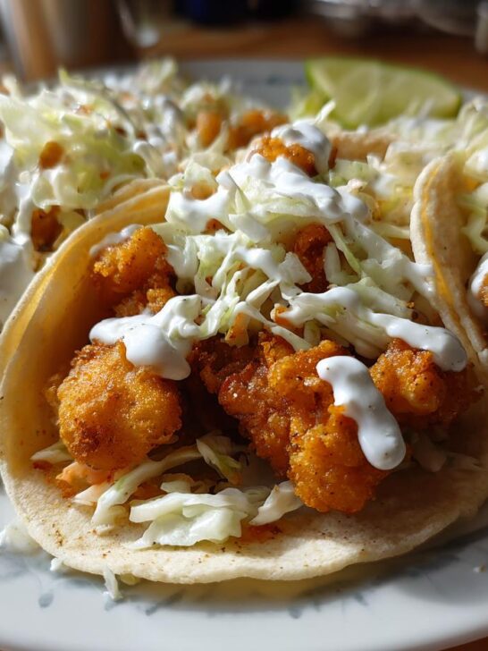 Three close-up Epic Baja Fish Tacos filled with crispy fried fish, shredded cabbage, and drizzled with white crema.