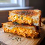Two halves of My Favorite Buffalo Chicken Melt Sandwich stacked, showing gooey orange buffalo chicken filling and melted cheese.