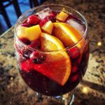 Close-up of a glass filled with Festive Christmas Sangria, featuring orange slices, cranberries, apple chunks, and ice cubes.