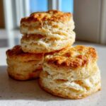 A stack of three golden brown, flaky Honey Buttermilk Biscuits showing distinct layers.