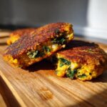 Close-up of a Flaky Jamaican Curry Chickpea Kale Veggie Patty cut in half, showing the golden crust and green kale filling.