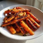A close-up of beautifully caramelized Garlic Herb Roasted Carrots piled in a white bowl.