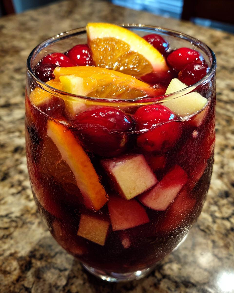 Close-up of a glass filled with Festive Christmas Sangria, loaded with cranberries, orange slices, and diced apples.