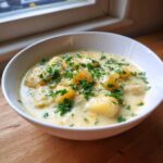 A close-up of a white bowl filled with Hearty Cheddar Garlic Herb Potato Soup, topped with fresh parsley.