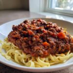 A close-up of rich, dark red Homemade Bolognese Sauce generously spooned over a bed of fettuccine pasta.