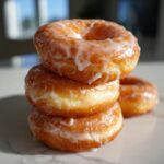 A stack of three golden, fluffy Homemade Classic Glazed Doughnuts dripping with sweet white icing.