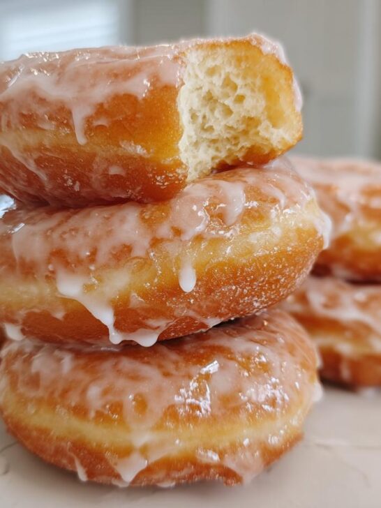 A stack of fluffy Homemade Classic Glazed Doughnuts, with the top one broken open showing the airy interior.