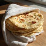 A stack of freshly made Homemade Flour Corn Tortillas wrapped in a white cloth to stay warm.