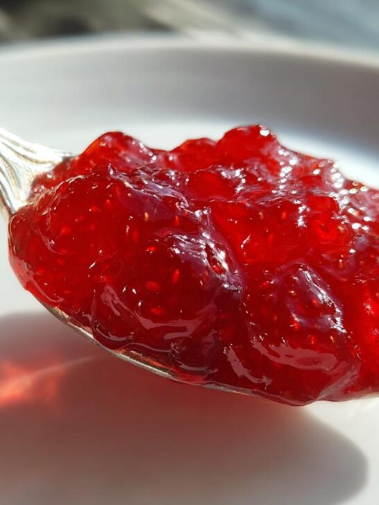 Close-up of a silver spoon holding a generous scoop of glistening, bright red Homemade Strawberry Jam.