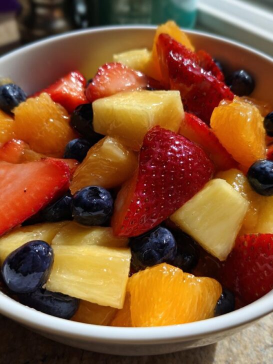 Close-up of a white bowl filled with vibrant Honey Lime Fruit Salad featuring strawberries, pineapple, oranges, and blueberries.