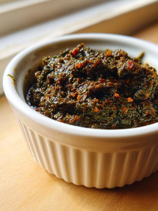 A close-up of thick, dark green Jamaican Jerk Seasoning Marinade in a small white ramekin.