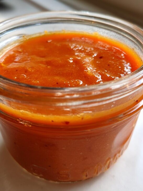 Close-up of bright orange Jamaican Scotch Bonnet Pepper Sauce filling a small glass mason jar.
