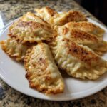 A close-up of several golden-brown, pan-fried Jerk Chicken Dumplings arranged on a white plate.