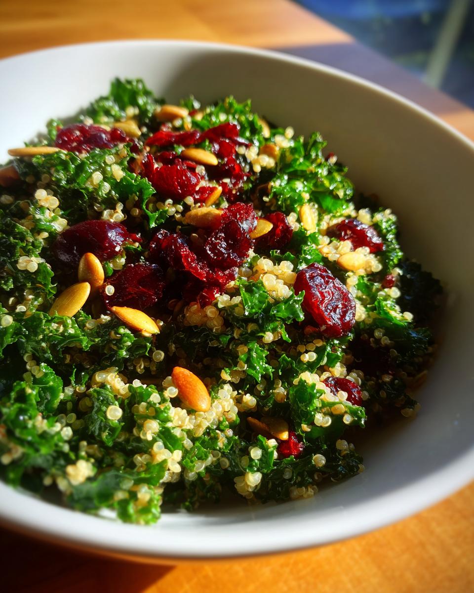 Close-up of a vibrant Kale Quinoa Salad topped with dried cranberries and mixed seeds in a white bowl.