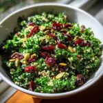 Close-up of a vibrant Kale Quinoa Salad mixed with dried cranberries and pumpkin seeds in a white bowl.