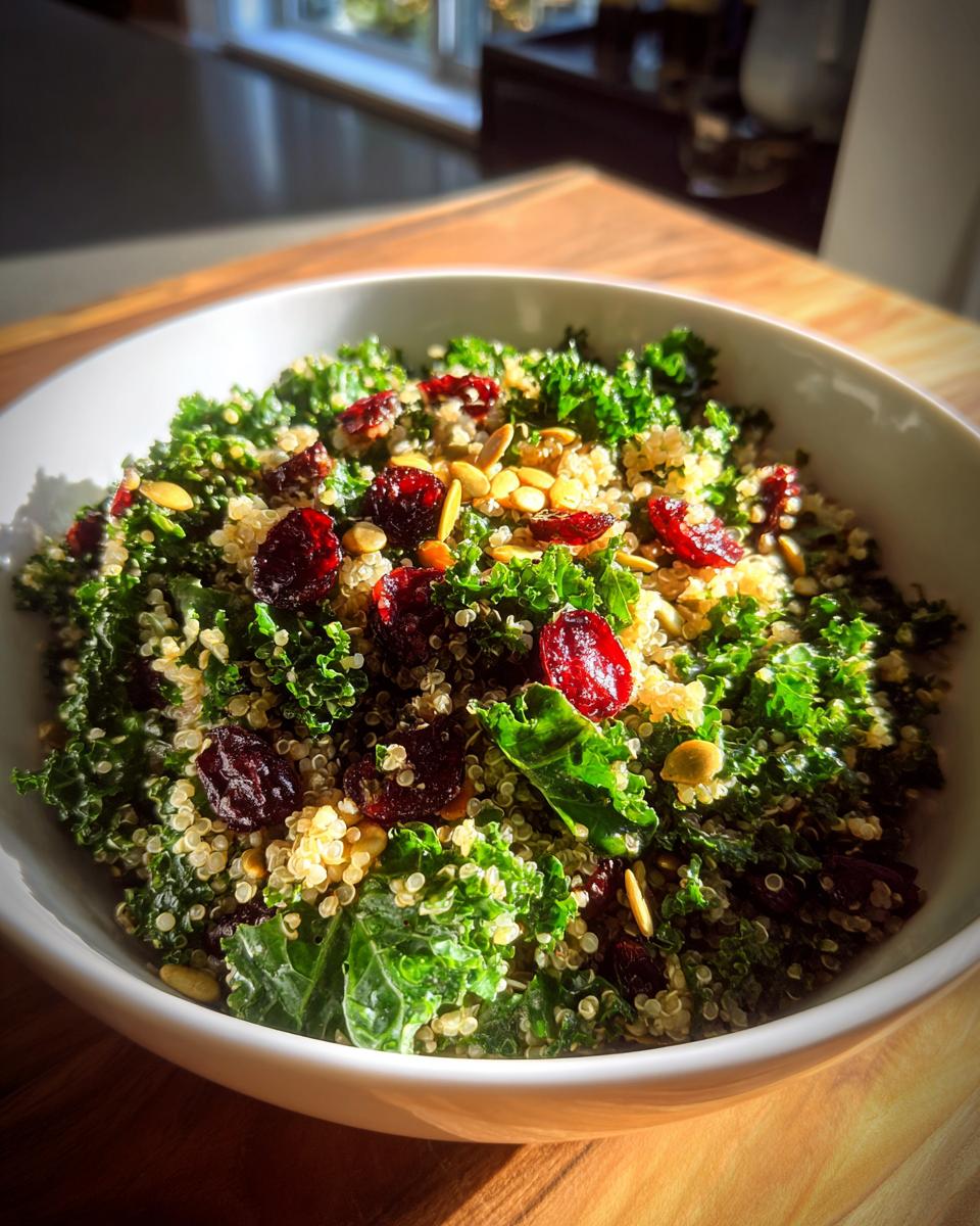 Close-up of a bright Kale Quinoa Salad mixed with dried cranberries and pumpkin seeds in a white bowl.