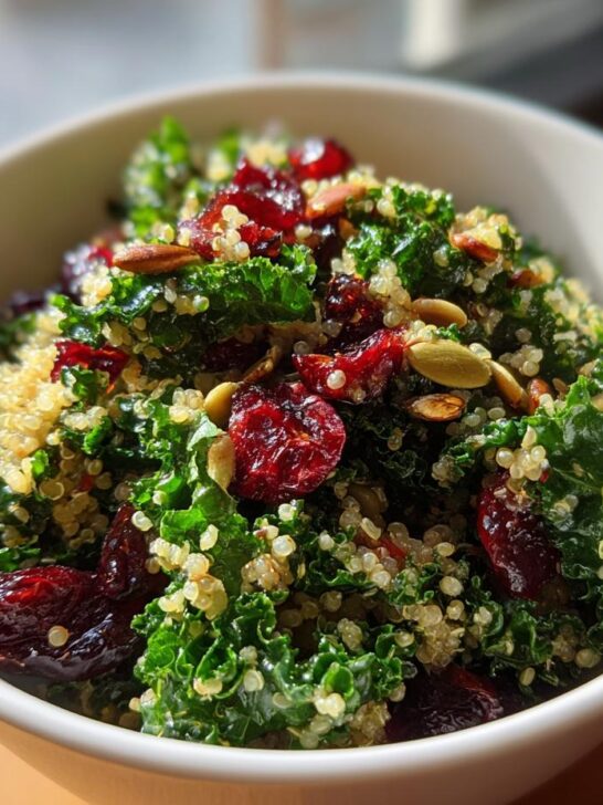 Close-up of a bowl filled with Kale Quinoa Salad featuring bright green kale, fluffy quinoa, dried cranberries, and pumpkin seeds.