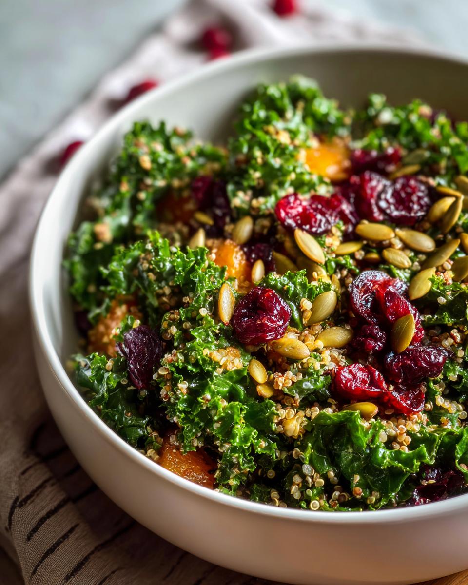A close-up of a vibrant Kale Quinoa Salad featuring dark leafy greens, quinoa, dried cranberries, and pumpkin seeds.