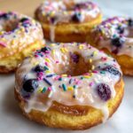 A close-up of a glazed Lemon Blueberry Doughnuts Sprinkles topped with colorful sprinkles and visible blueberries.
