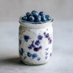 A glass jar filled with creamy Lemon Blueberry Overnight Oats, topped generously with fresh blueberries.