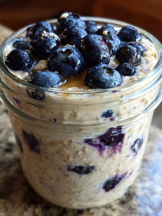 Close-up of Lemon Blueberry Overnight Oats in a glass jar, topped generously with fresh blueberries and a drizzle of syrup.