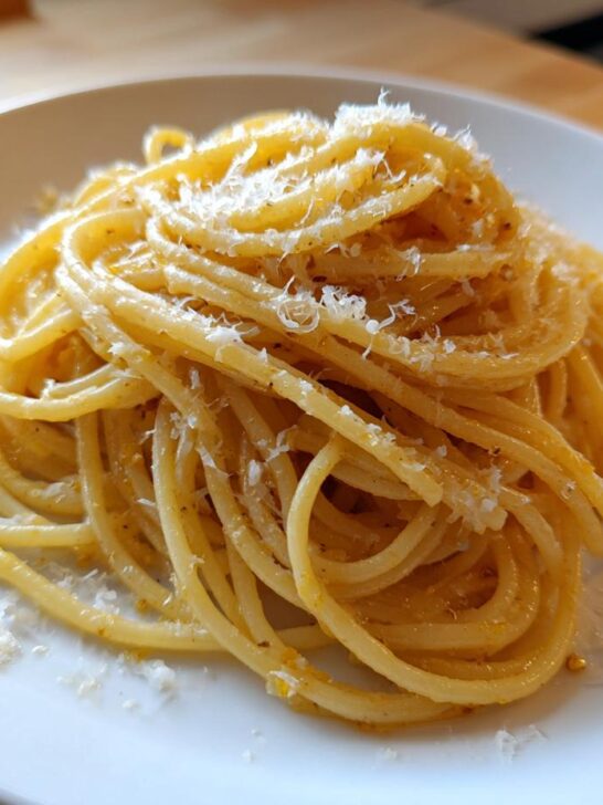 A close-up of perfectly twirled Lemon Brown Butter Spaghetti topped with grated Parmesan cheese on a white plate.