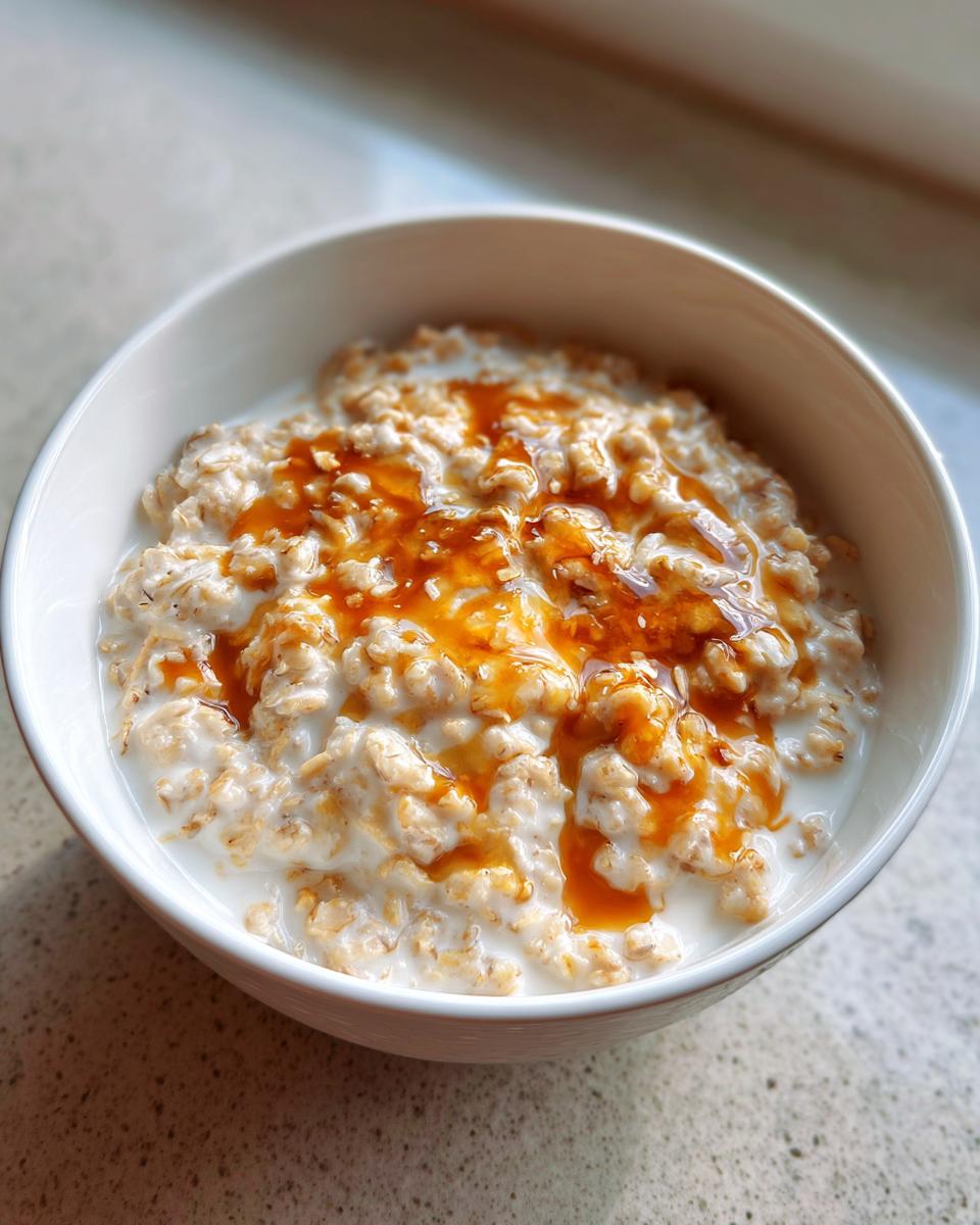 Close-up of a white bowl filled with creamy Maple Brown Sugar Oatmeal topped with a generous drizzle of amber syrup.
