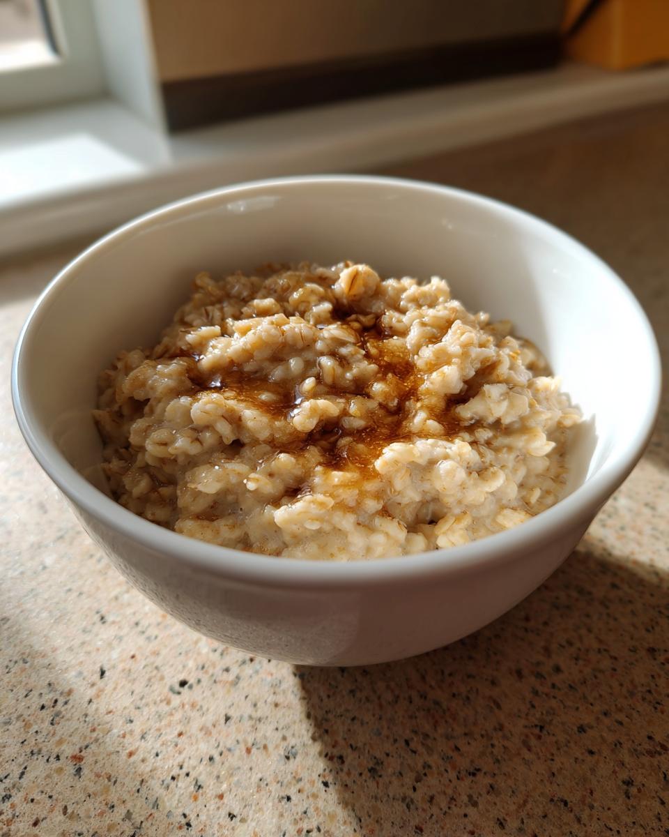 A close-up of warm Maple Brown Sugar Oatmeal in a white bowl, drizzled with syrup.