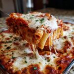 A serving of Meatless Baked Ziti With Ricotta Mozzarella being lifted, showing extreme cheese pull and melted mozzarella topping.