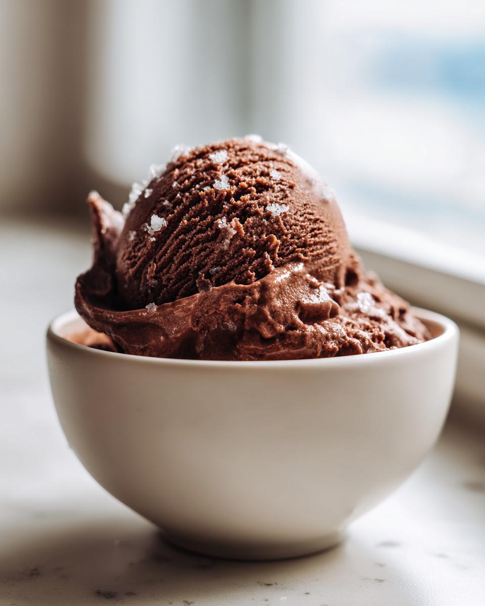 A rich scoop of dark chocolate Mocha Latte Frozen Yogurt topped with flaky sea salt in a white bowl.