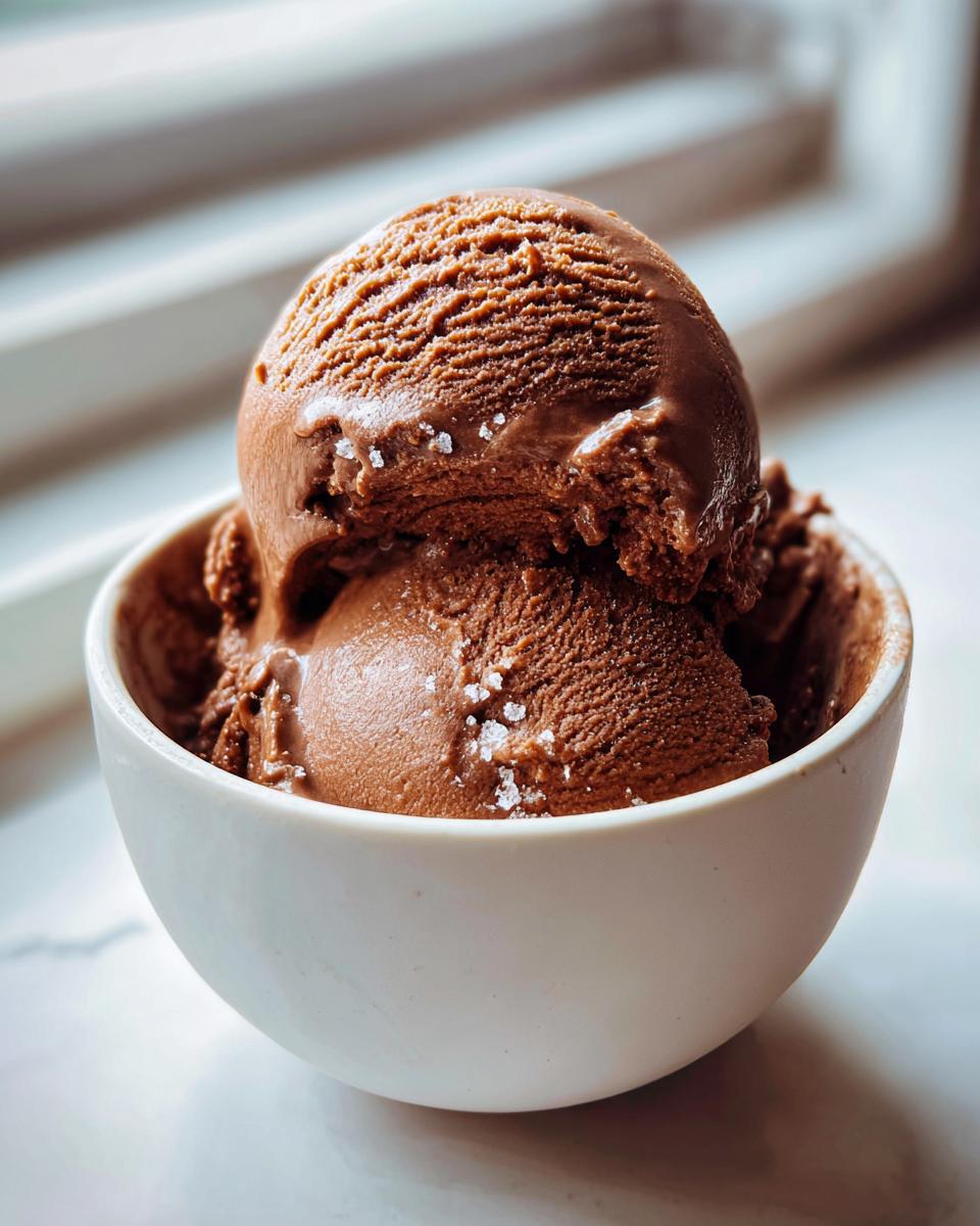 Two scoops of rich brown Mocha Latte Frozen Yogurt sprinkled with flaky sea salt in a white bowl.