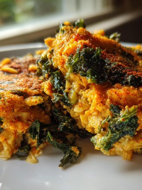 Close-up of two servings of Nashville Hot Cauliflower Kale Grits, showing yellow grits mixed with dark green kale and dusted with red spice.
