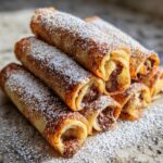A close-up stack of golden Nutella French Toast Rollups dusted heavily with powdered sugar.