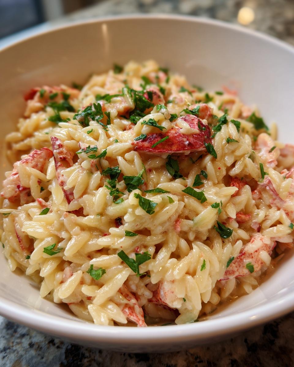 A close-up view of a white bowl filled with One Pot Creamy Lobster Orzo, topped with fresh parsley.