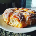 A cluster of freshly baked Orange Glazed Sweet Dinner Rolls drizzled with white icing, sitting on a white plate.