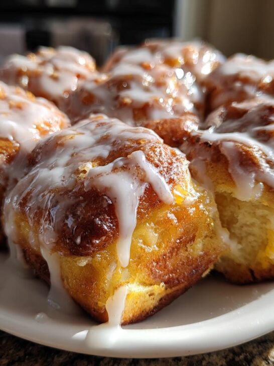 A plate of freshly baked Orange Glazed Sweet Dinner Rolls dripping with white icing.