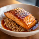 Close-up of a perfectly cooked fillet of salmon with a sesame seed glaze served over a bed of farro in a bowl.