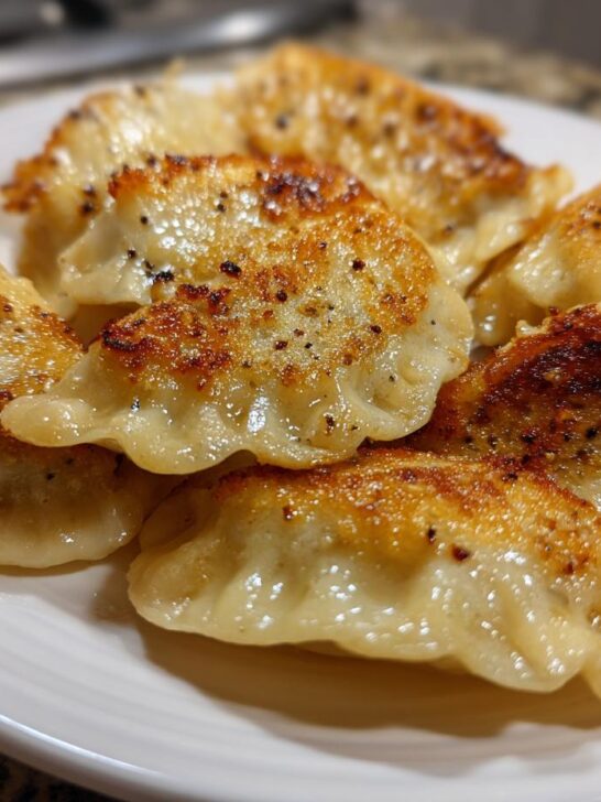Close-up of several golden, pan-fried Jerk Chicken Dumplings seasoned with pepper on a white plate.