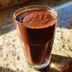 Close-up of a thick, dark brown Peanut Butter Cup Smoothie served in a clear glass on a granite countertop.