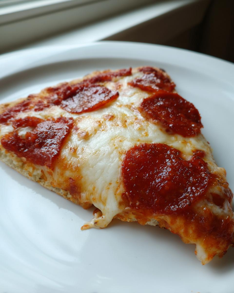 Close-up of a single slice of pepperoni Flatbread Pizza with bubbly, melted mozzarella cheese on a white plate.