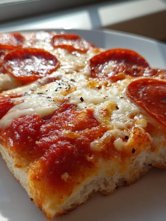 Two slices of thick, cheesy pepperoni Flatbread Pizza resting on a white plate in bright sunlight.